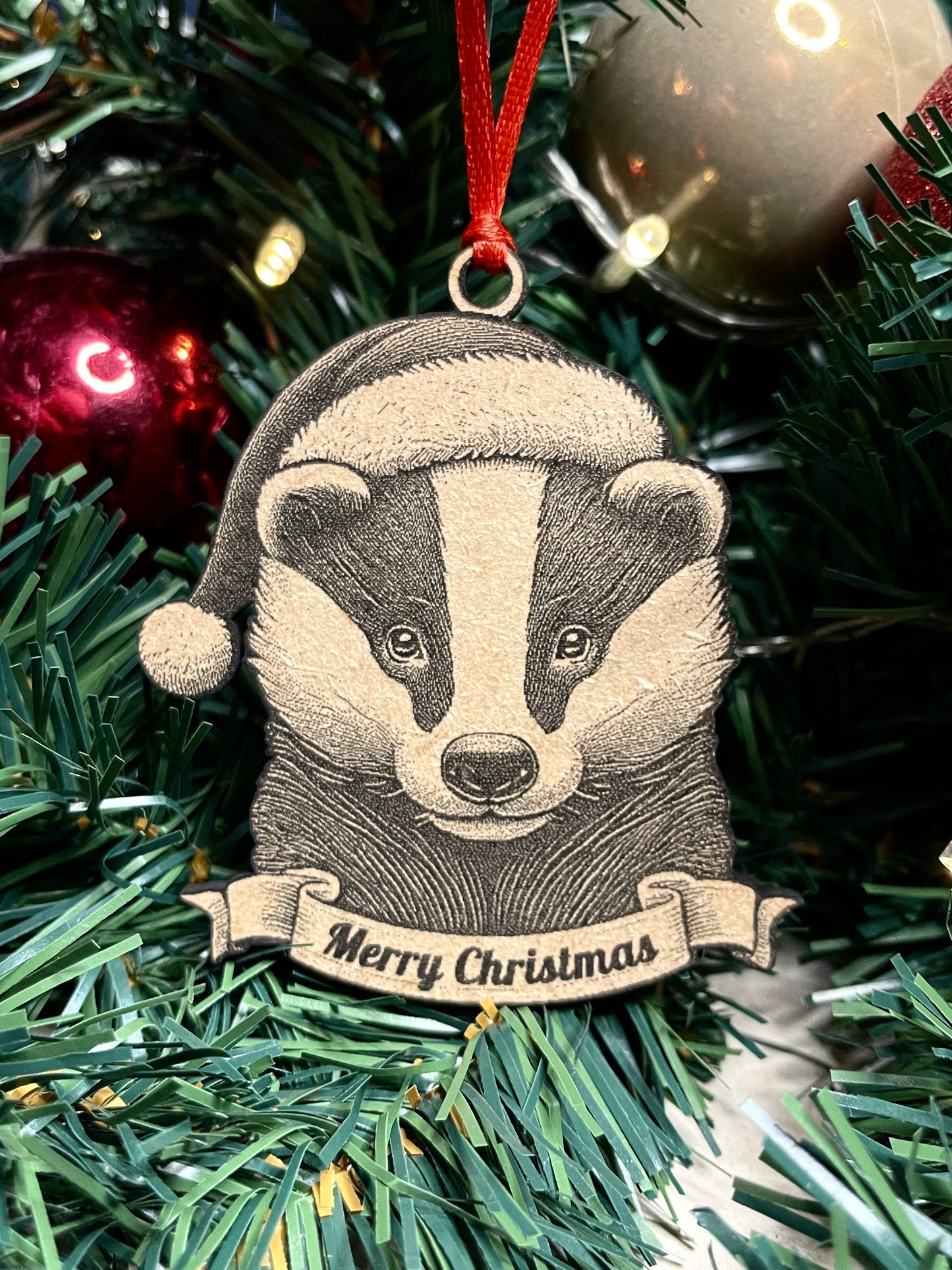 A badger tree ornament with a Santa hat and a banner that reads 'Merry Christmas', 