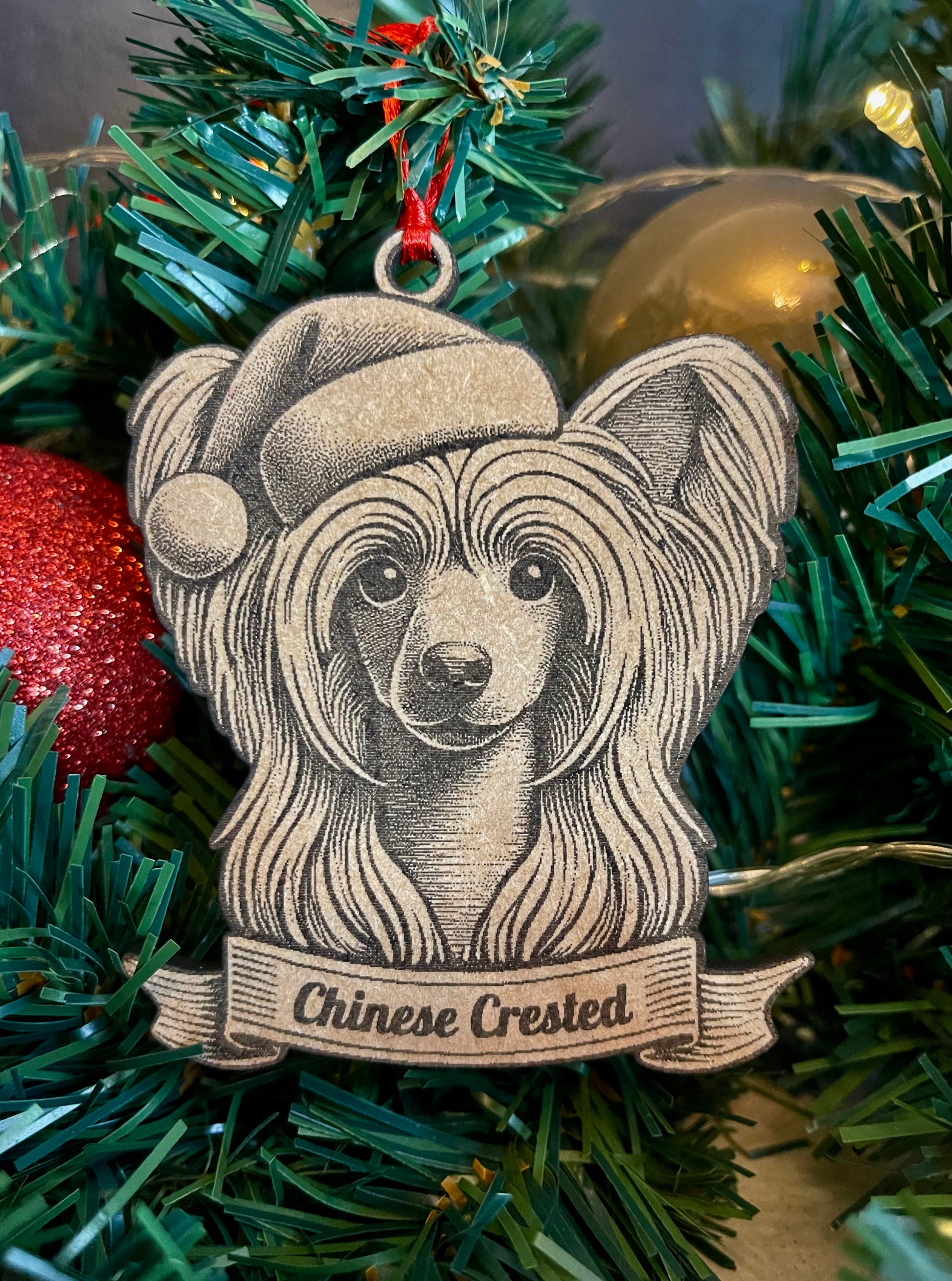 A wooden ornament in the shape of a Chinese Crested dog wearing a Santa hat, hanging on a Christmas tree.