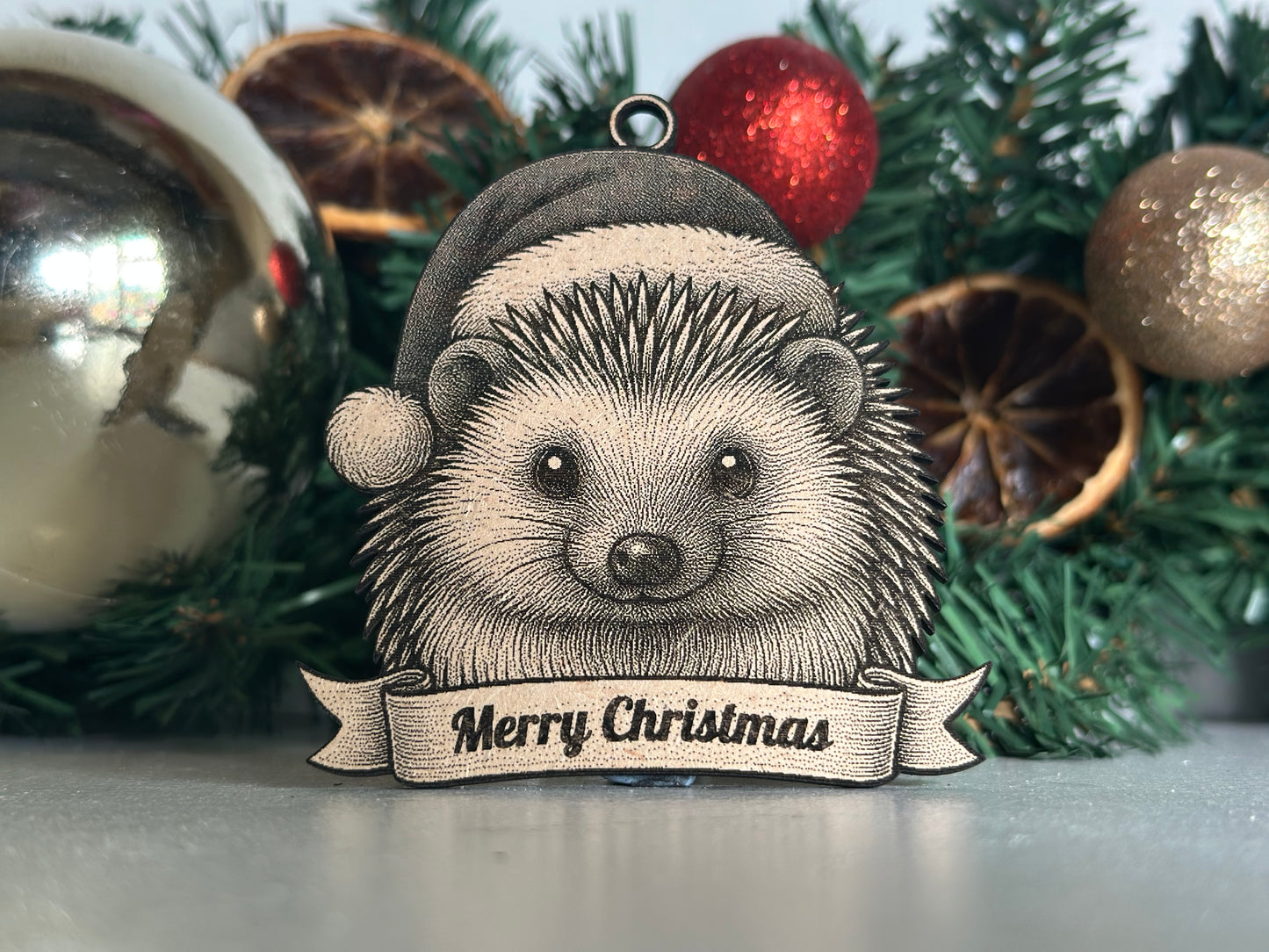 Decorative ornament of a hedgehog with a 'Merry Christmas' banner on a Christmas tree.