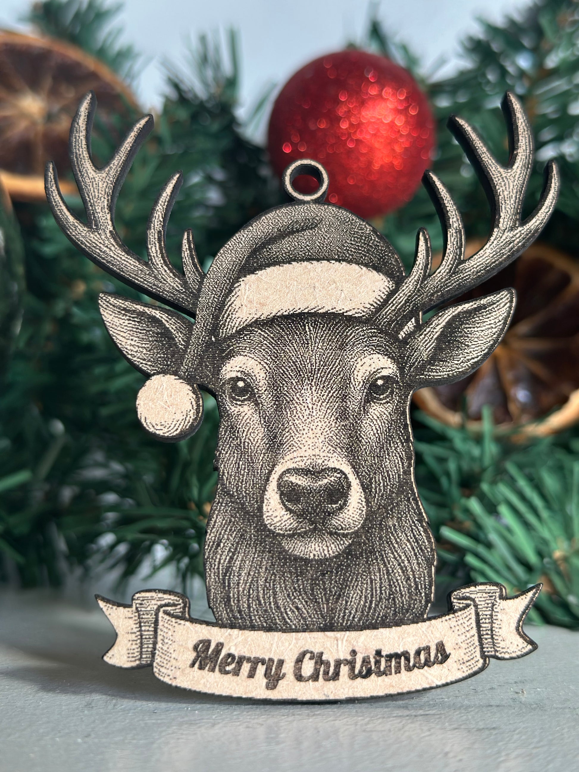 Decorative Stag ornament with 'Merry Christmas' banner on a Christmas tree.