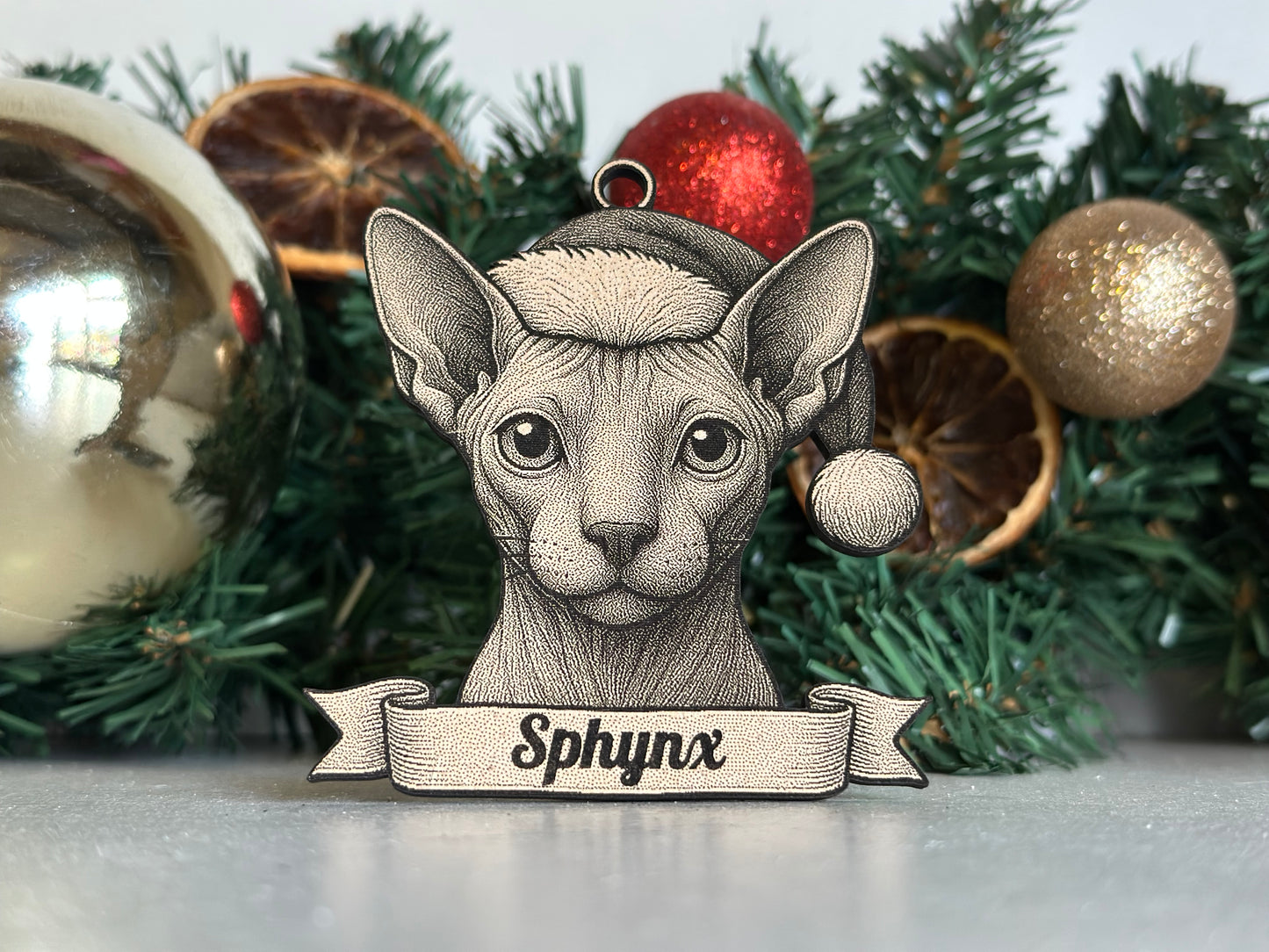 Decorative cat ornament with 'Sphynx' text on a Christmas tree with ornaments and pine needles.