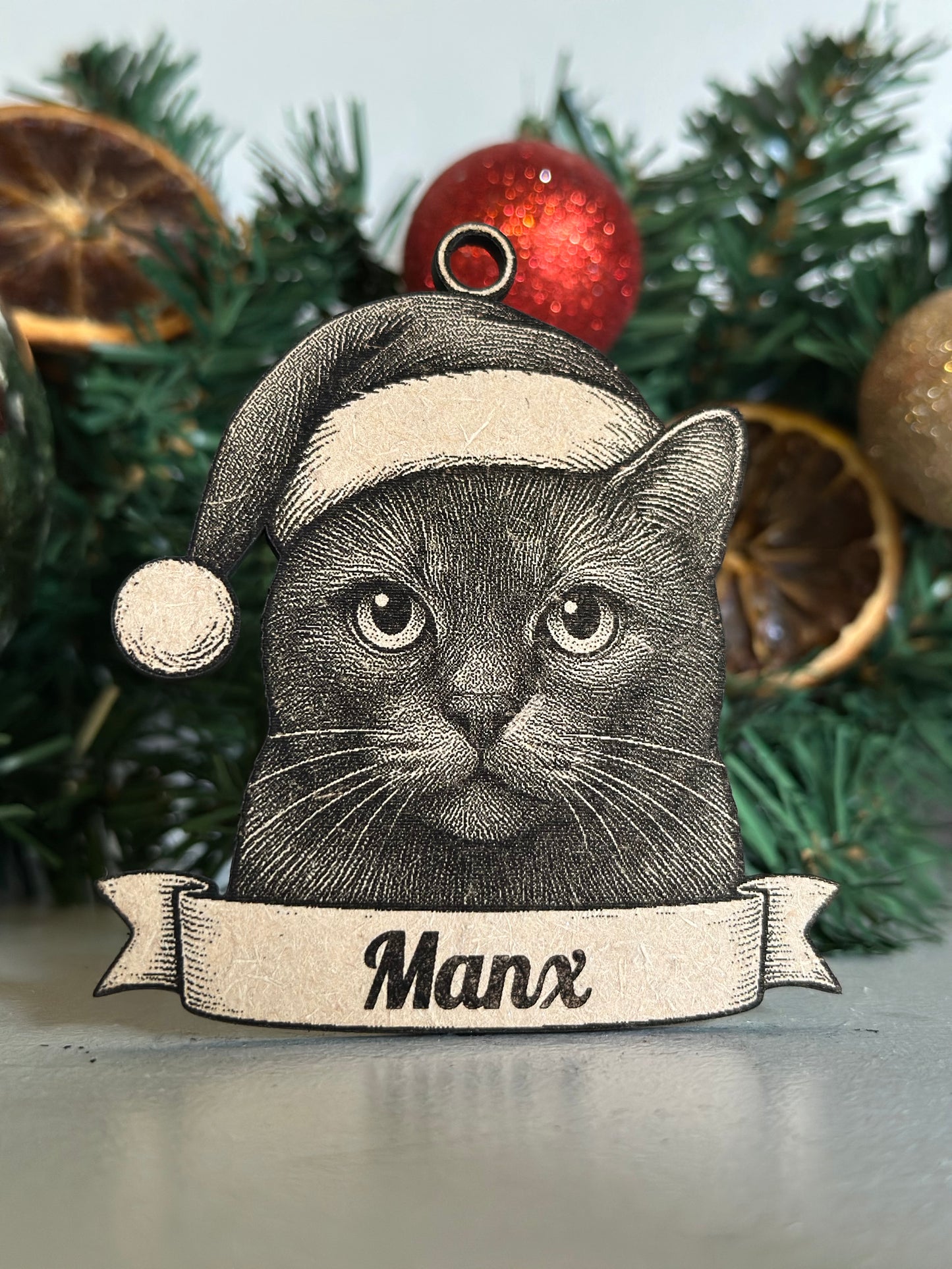Decorative Christmas ornament with a cat design and 'Manx' banner, placed on a Christmas tree.