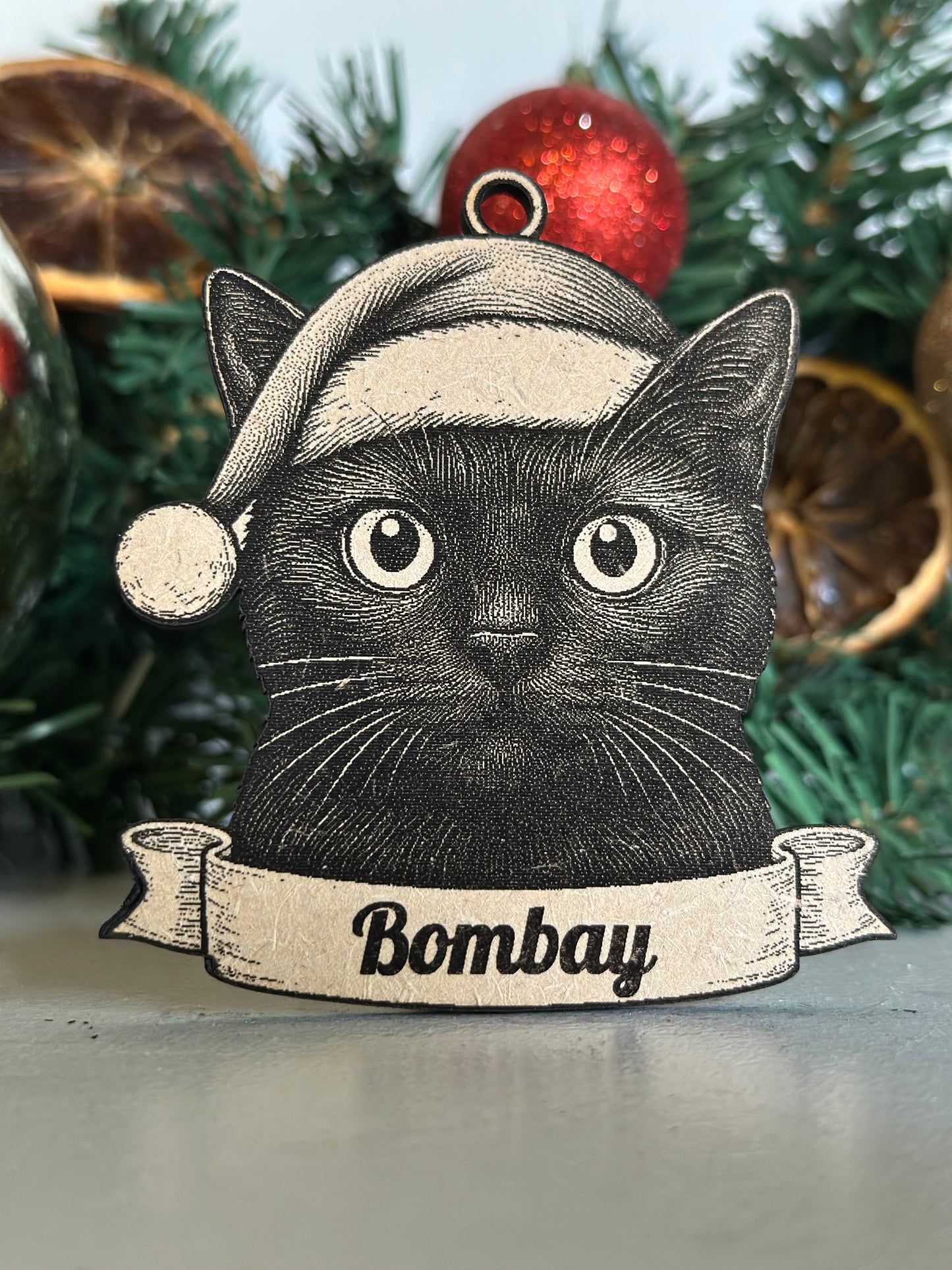 Decorative Christmas ornament with a black cat illustration and 'Bombay' text on a green wreath.