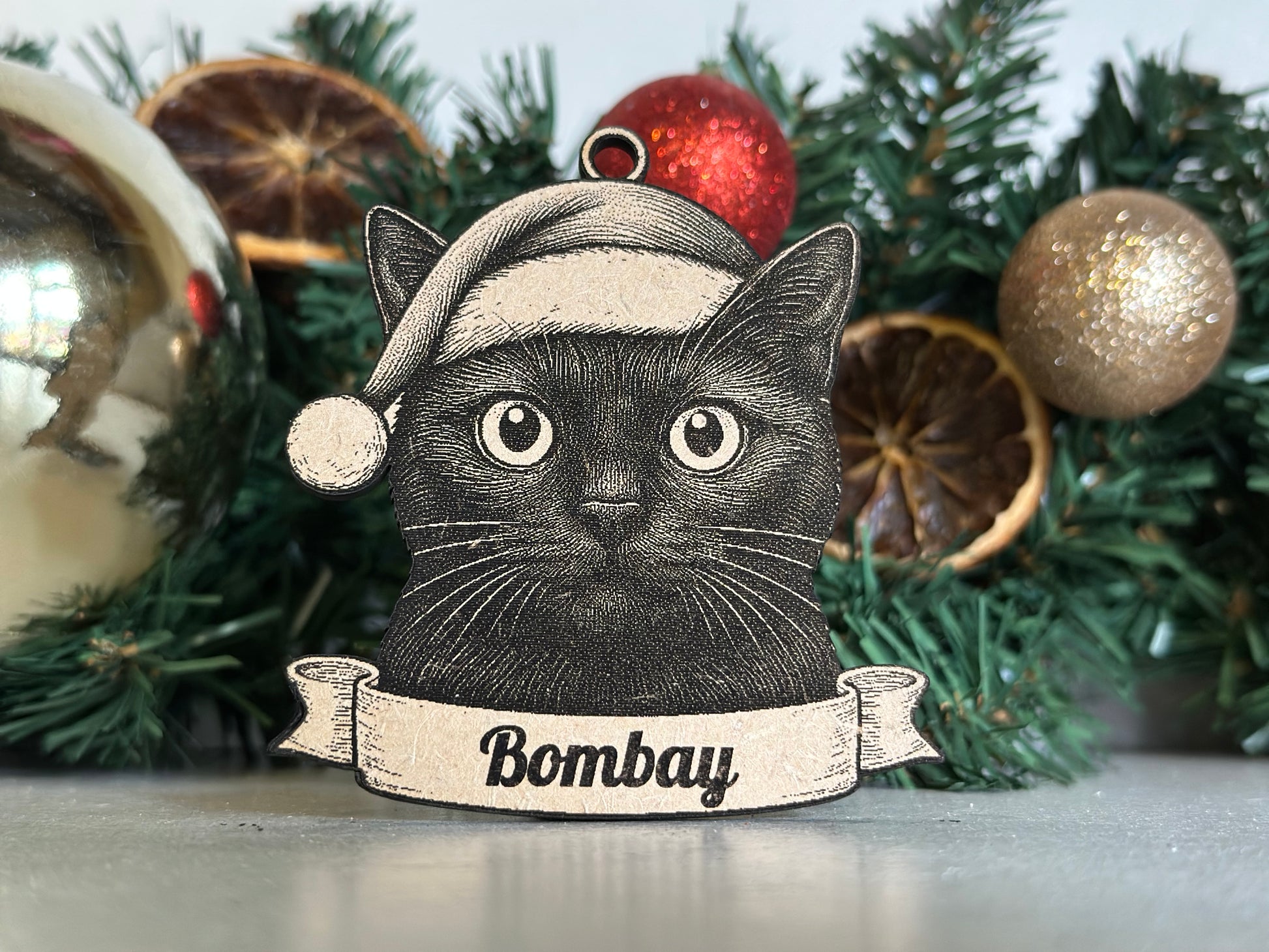 Decorative Christmas ornament with a black cat design and 'bombay' text, set against a festive background.