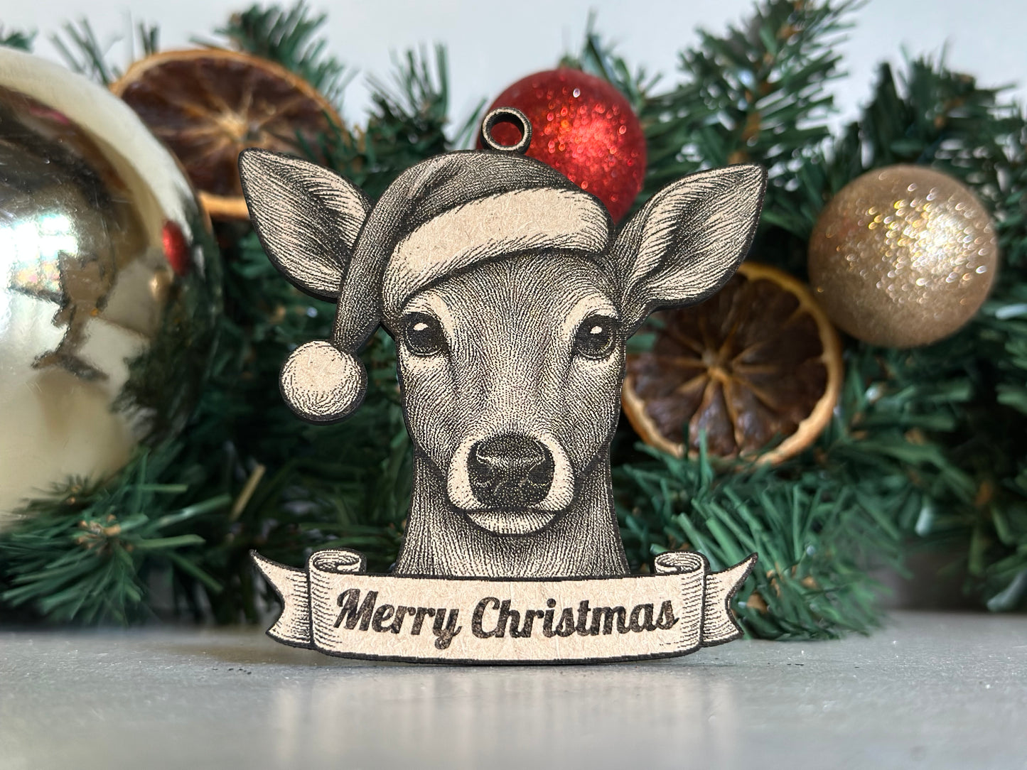 Decorative deer / doe ornament with 'Merry Christmas' banner on a green wreath with ornaments.