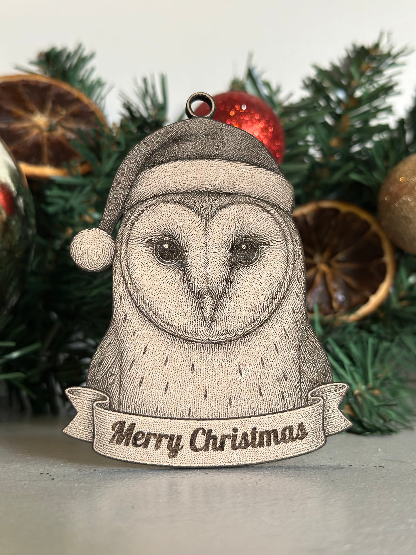 Ornament with an owl design wearing a Santa hat and 'Merry Christmas' banner, set against a Christmas tree background.