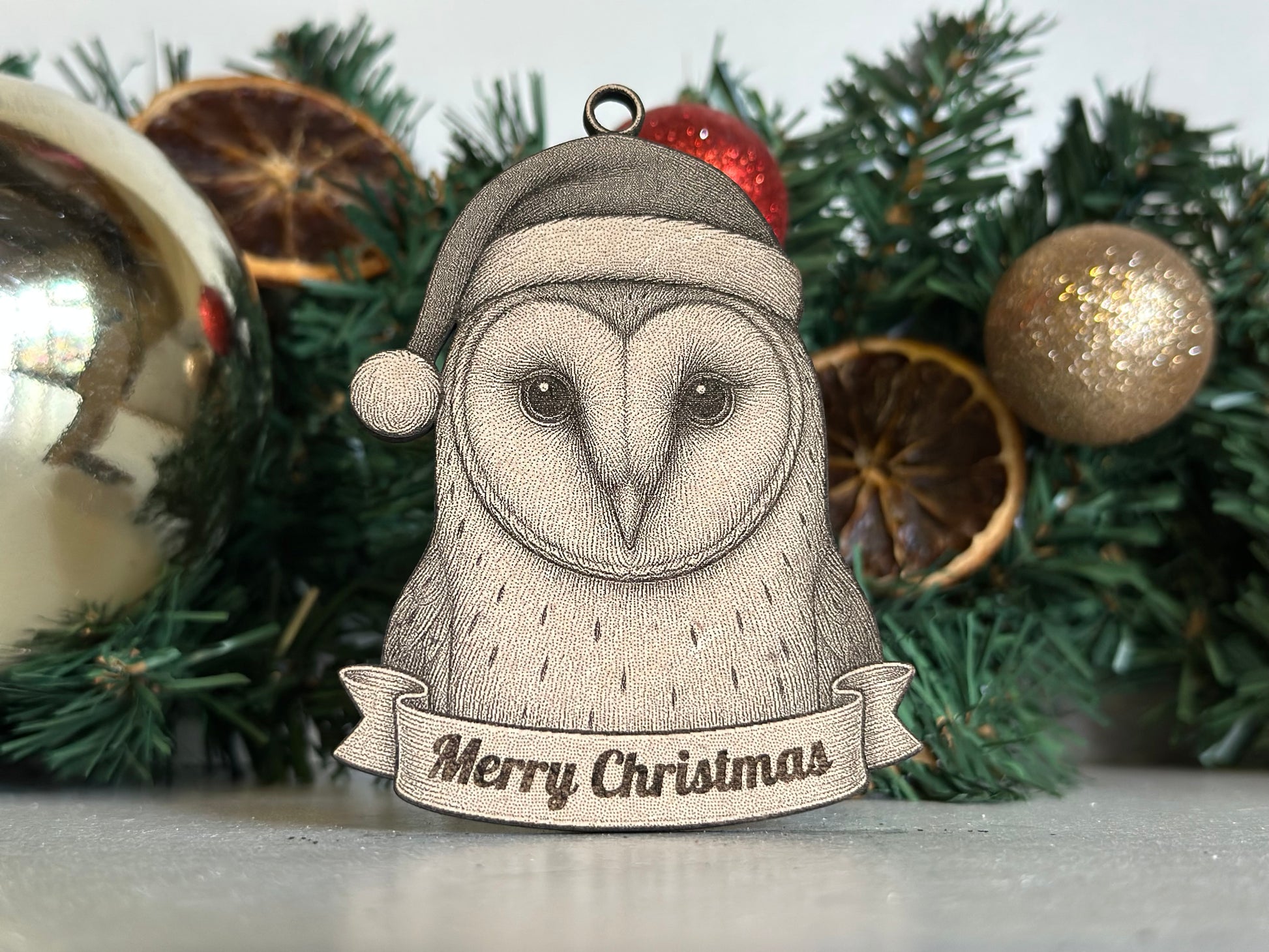 Ornament with owl design wearing a Santa hat and 'Merry Christmas' banner, set against a festive background.