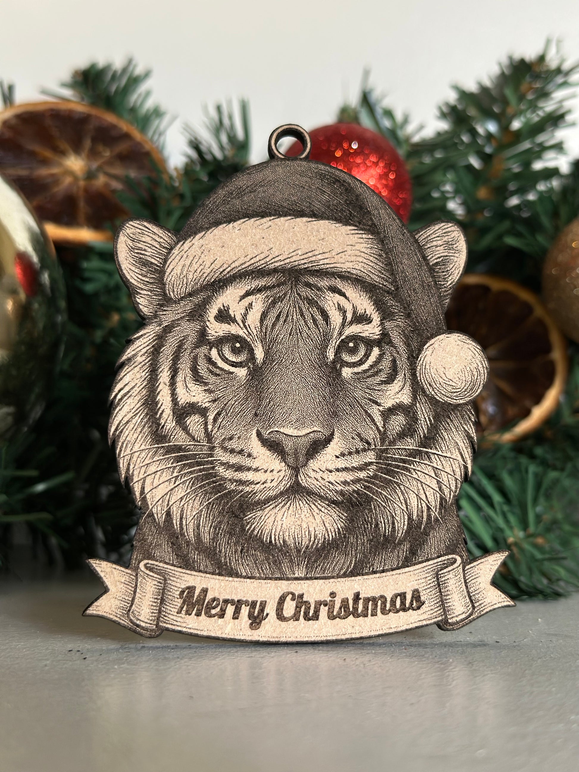 Tiger Christmas ornament with Santa hat and 'Merry Christmas' banner against a festive background.