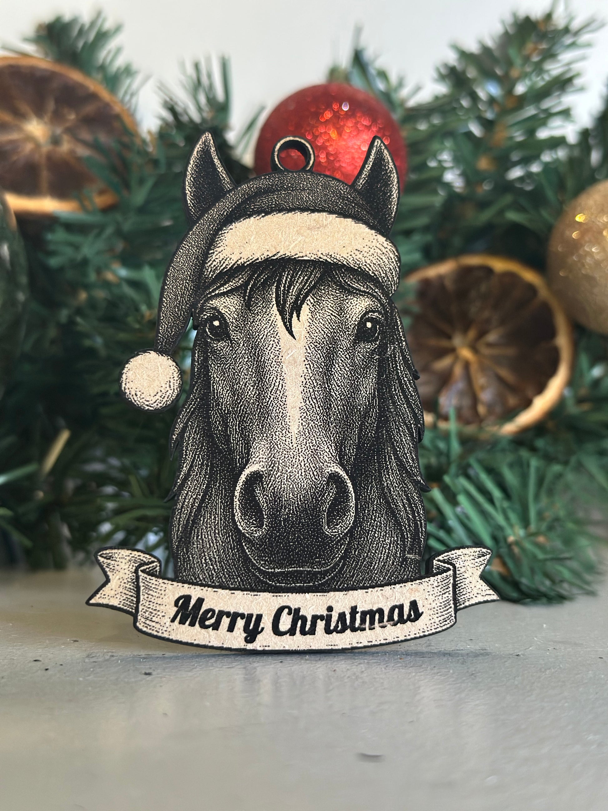 Decorative horse ornament with 'Merry Christmas' banner on a Christmas tree.
