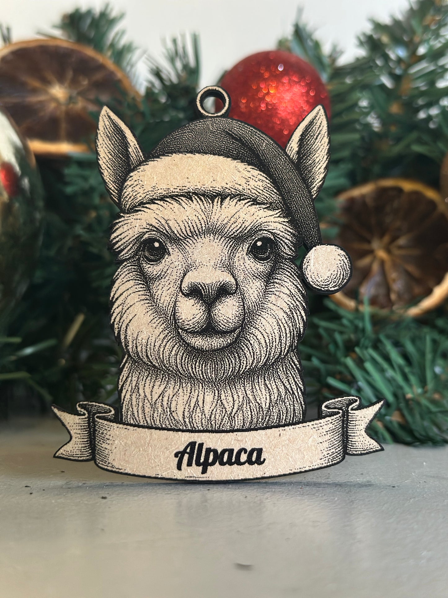 Decorative ornament of an alpaca wearing a Santa hat with Christmas decorations in the background.