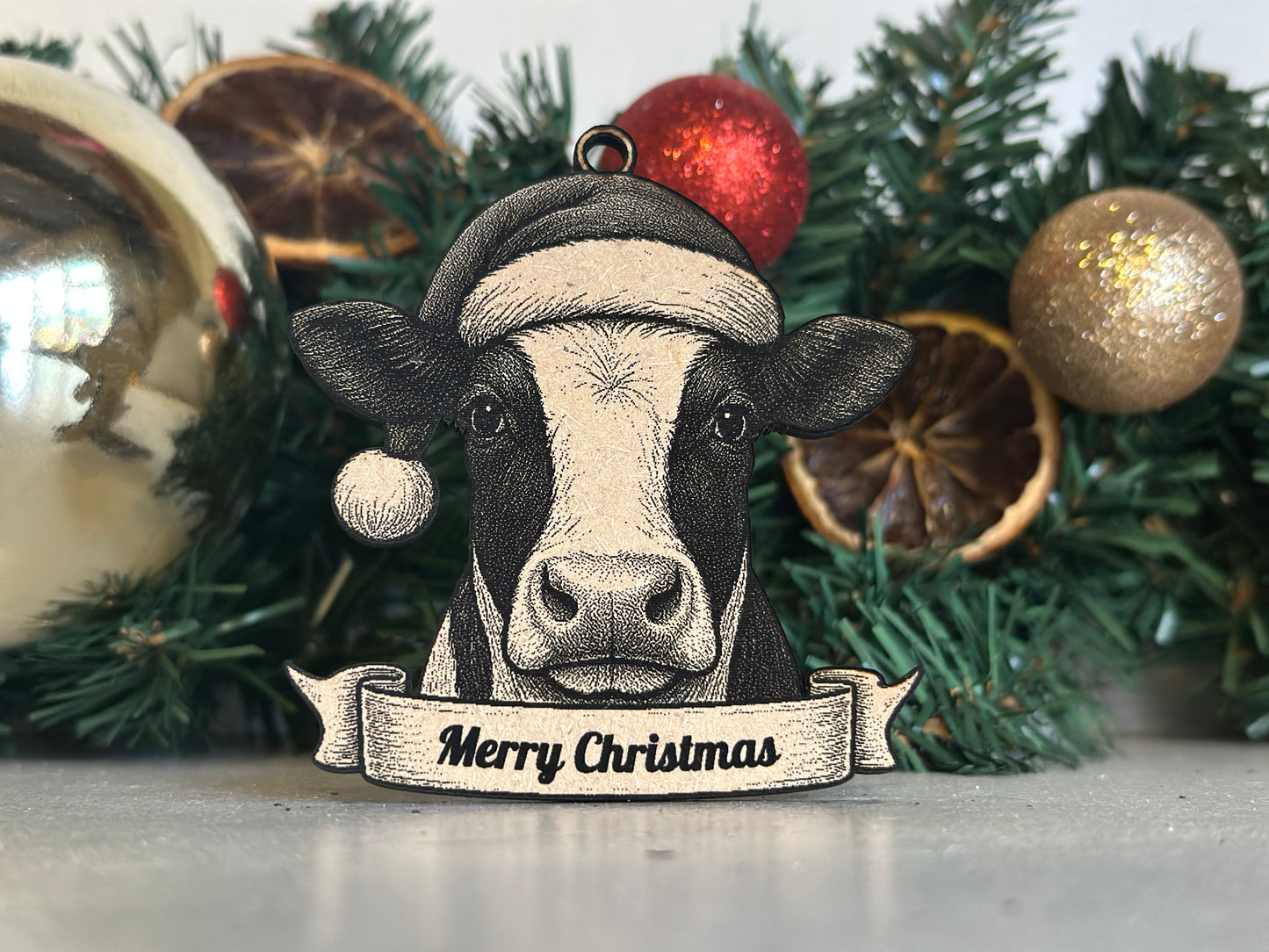 Decorative cow ornament with a Christmas hat and 'Merry Christmas' banner against a festive background.