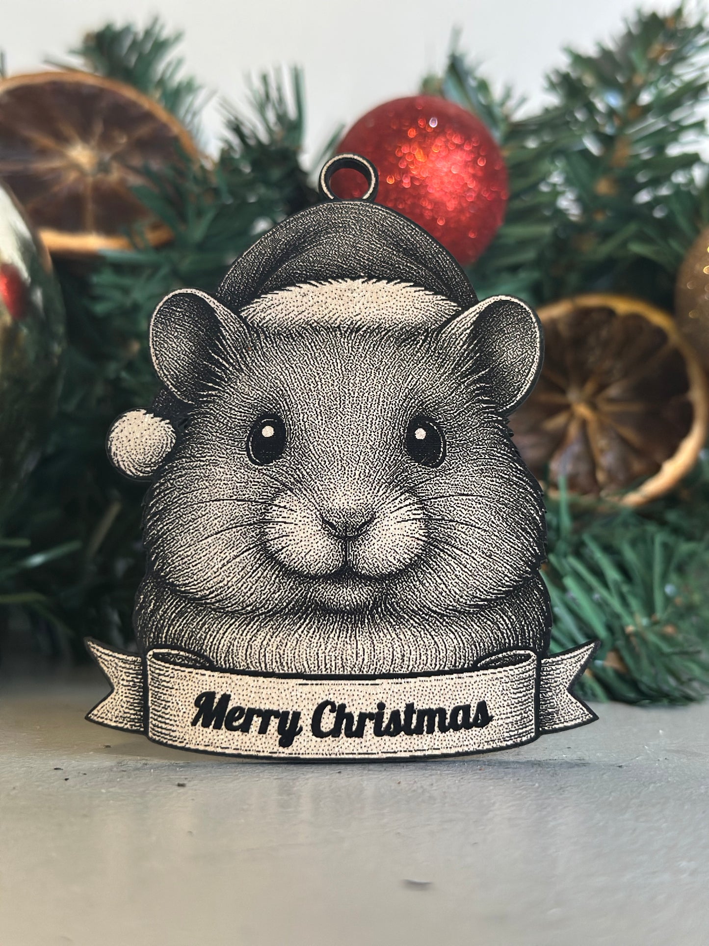 Decorative hamster ornament with 'Merry Christmas' banner on a Christmas tree.