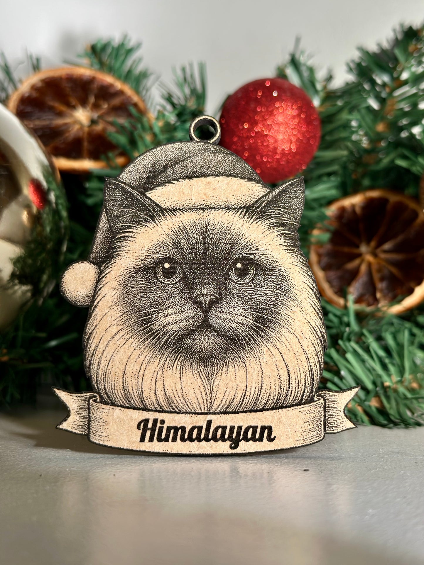 Decorative ornament with a Himalayan cat design against a Christmas-themed background.