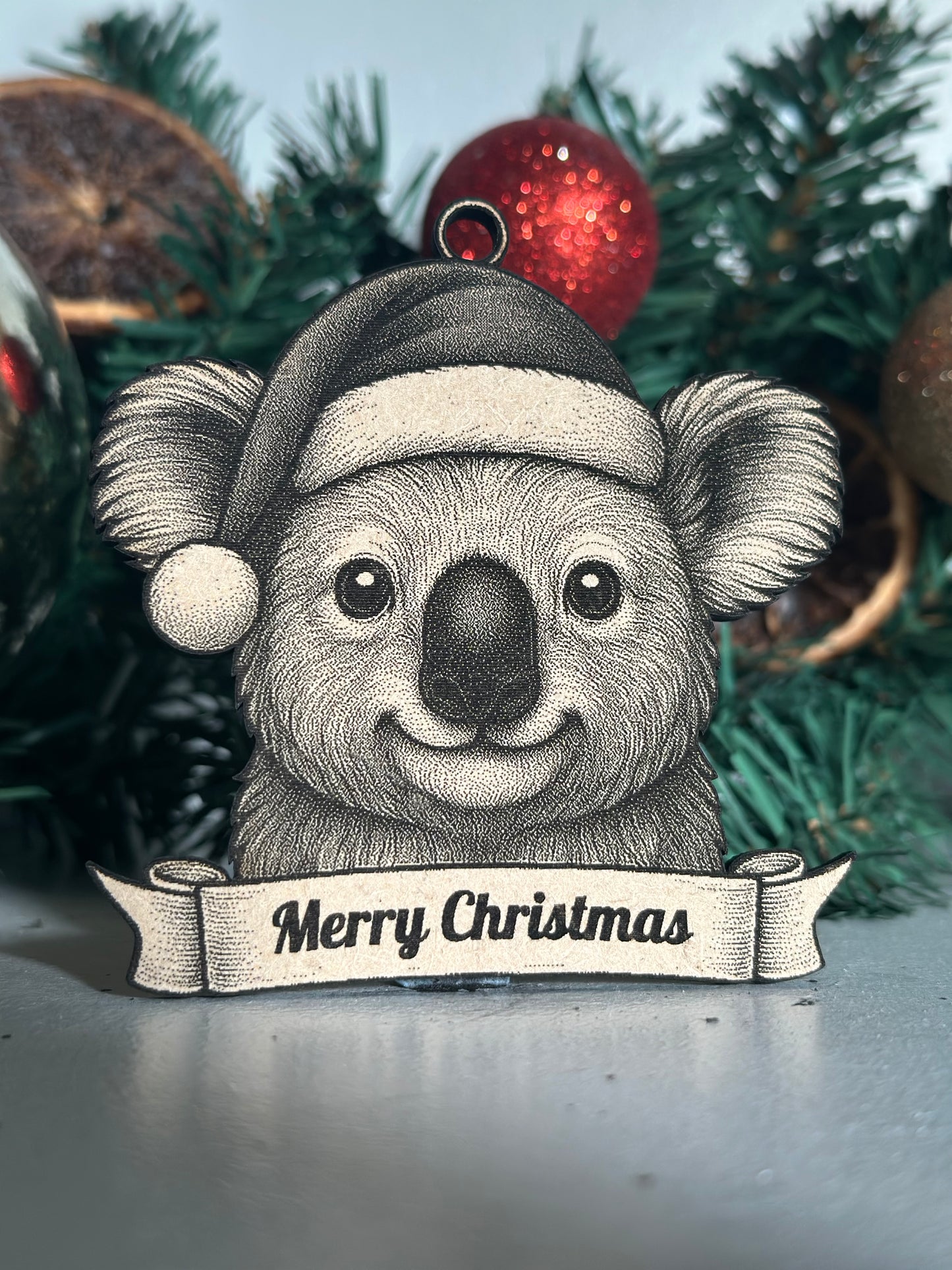 Decorative koala ornament with 'Merry Christmas' banner on a Christmas tree.