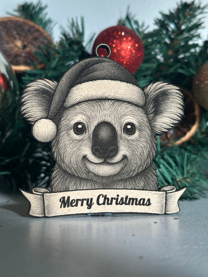 Decorative koala ornament with 'Merry Christmas' banner on a Christmas tree.